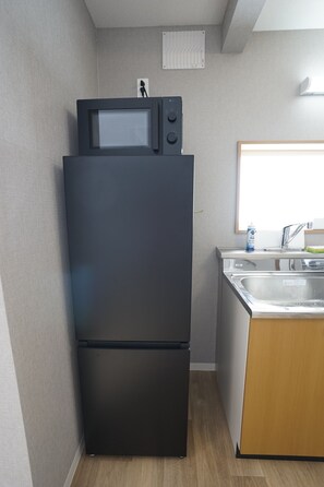 A compact kitchen with a black refrigerator, a microwave, a sink, and a window above the sink. - Yukimi Nakafurano (Sorachi-gun,Nakafurano-cho)