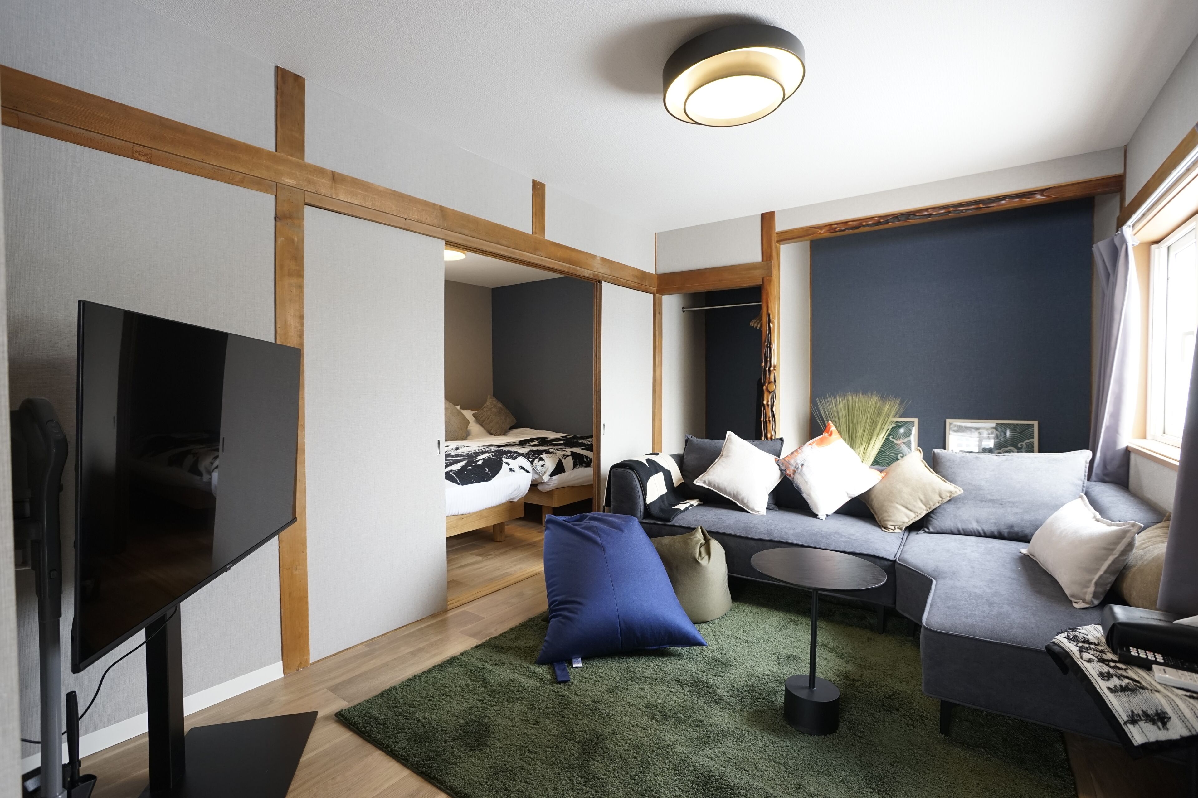Ein modernes Wohnzimmer mit einem Flachbildfernseher, einem grauen Sofa, einem kleinen runden Tisch und einem grünen Teppich.