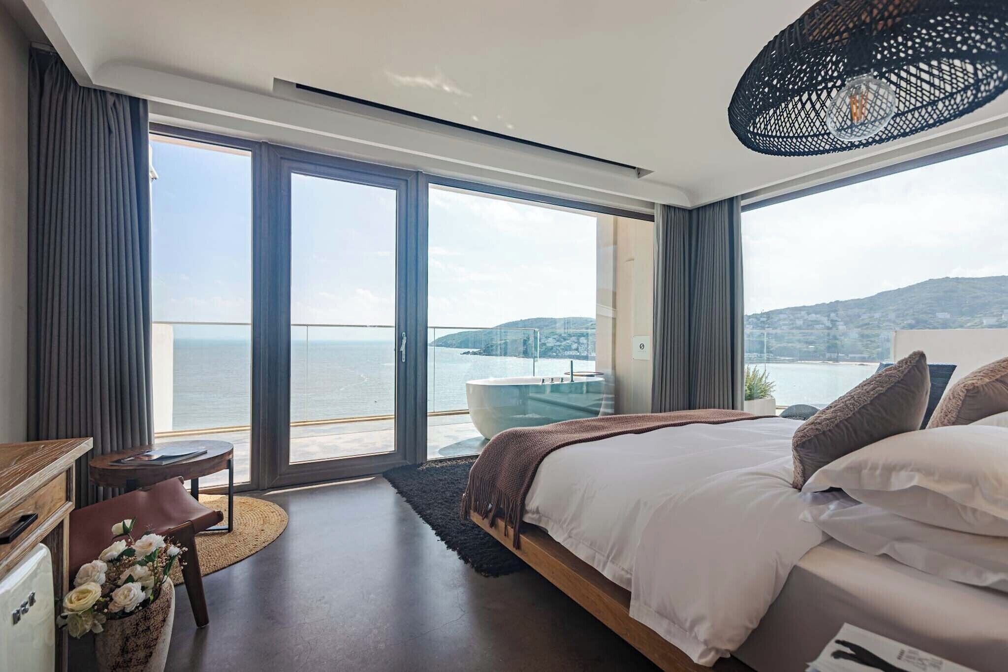 A modern bedroom with a large bed, a view of the sea, and a balcony with a glass door.