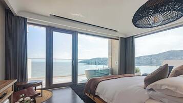 A modern bedroom with a large bed, a view of the sea, and a balcony with a glass door.
