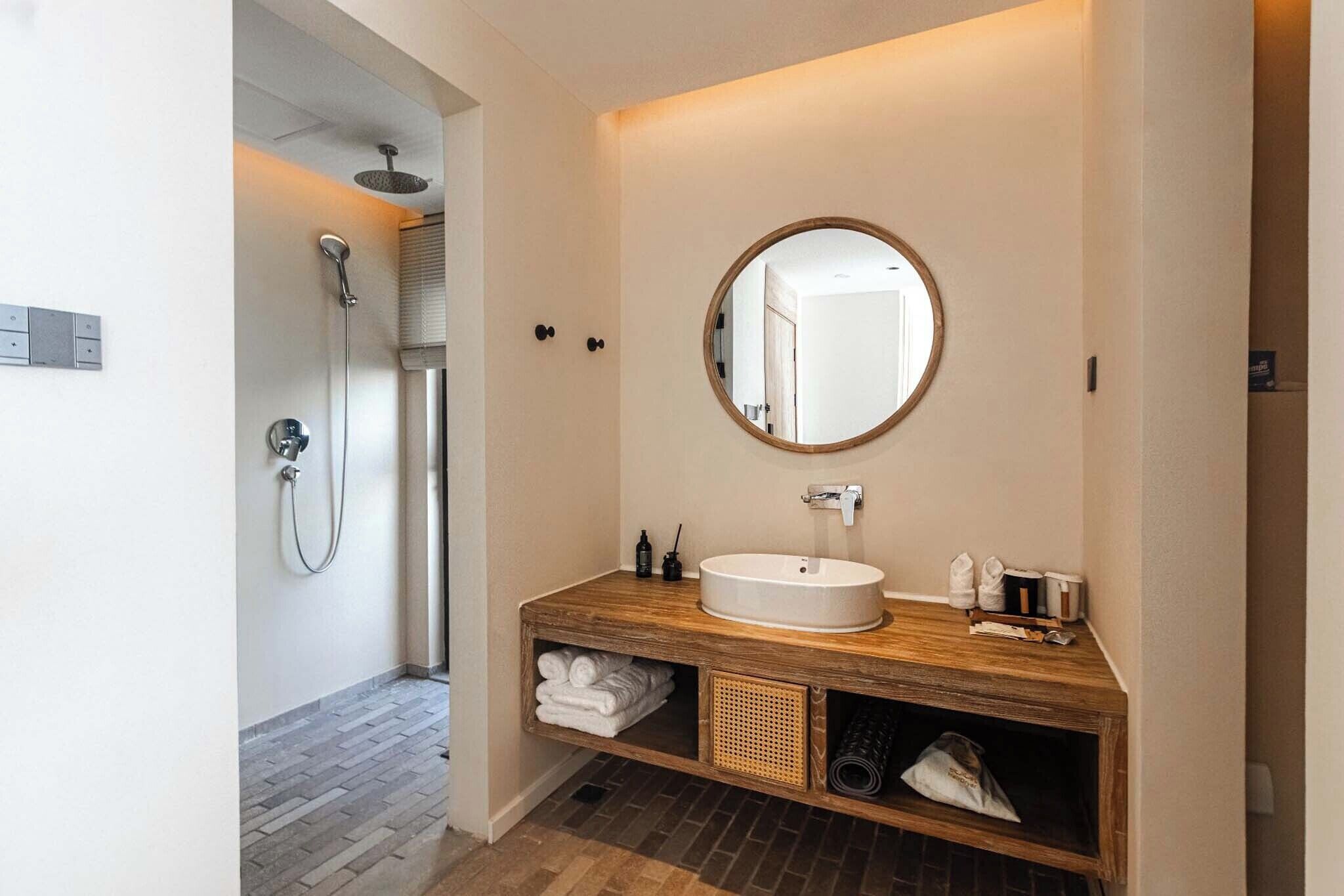 Un baño moderno con un mueble de tocador de madera, un espejo redondo y una ducha.