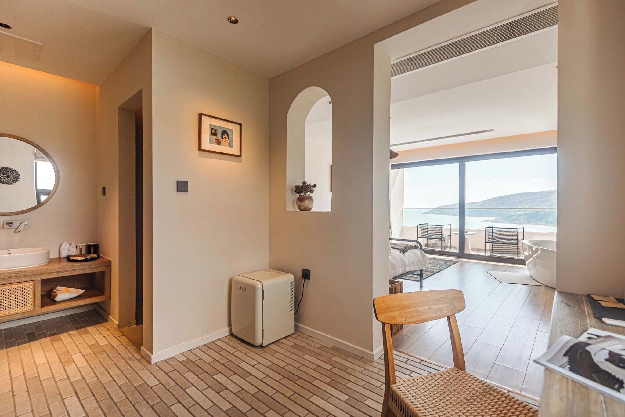 A modern bathroom with a sink, mirror, and heater, leading to a balcony with a view.