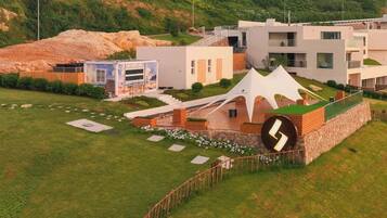 A modern building with a unique curved entrance, a large cylindrical structure, and a landscaped garden with pathways and flower beds.