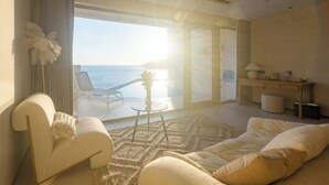 A modern living room with a large window overlooking the sea, a white sofa, a small table, and a lamp. - XIHUI Cliff Hotel (Zhoushan)