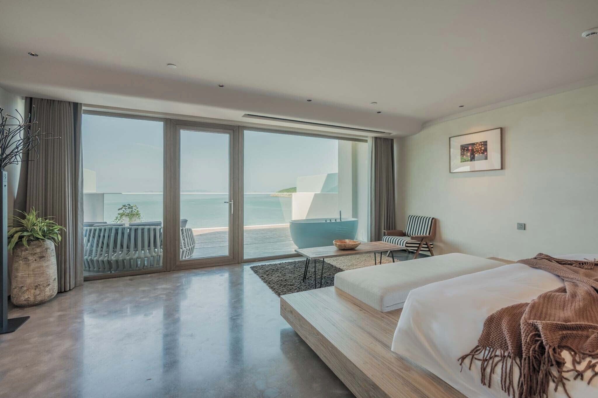 Een moderne hotelkamer met een grote schuifpui naar het balkon, een bed, een kleine tafel en een stoel.