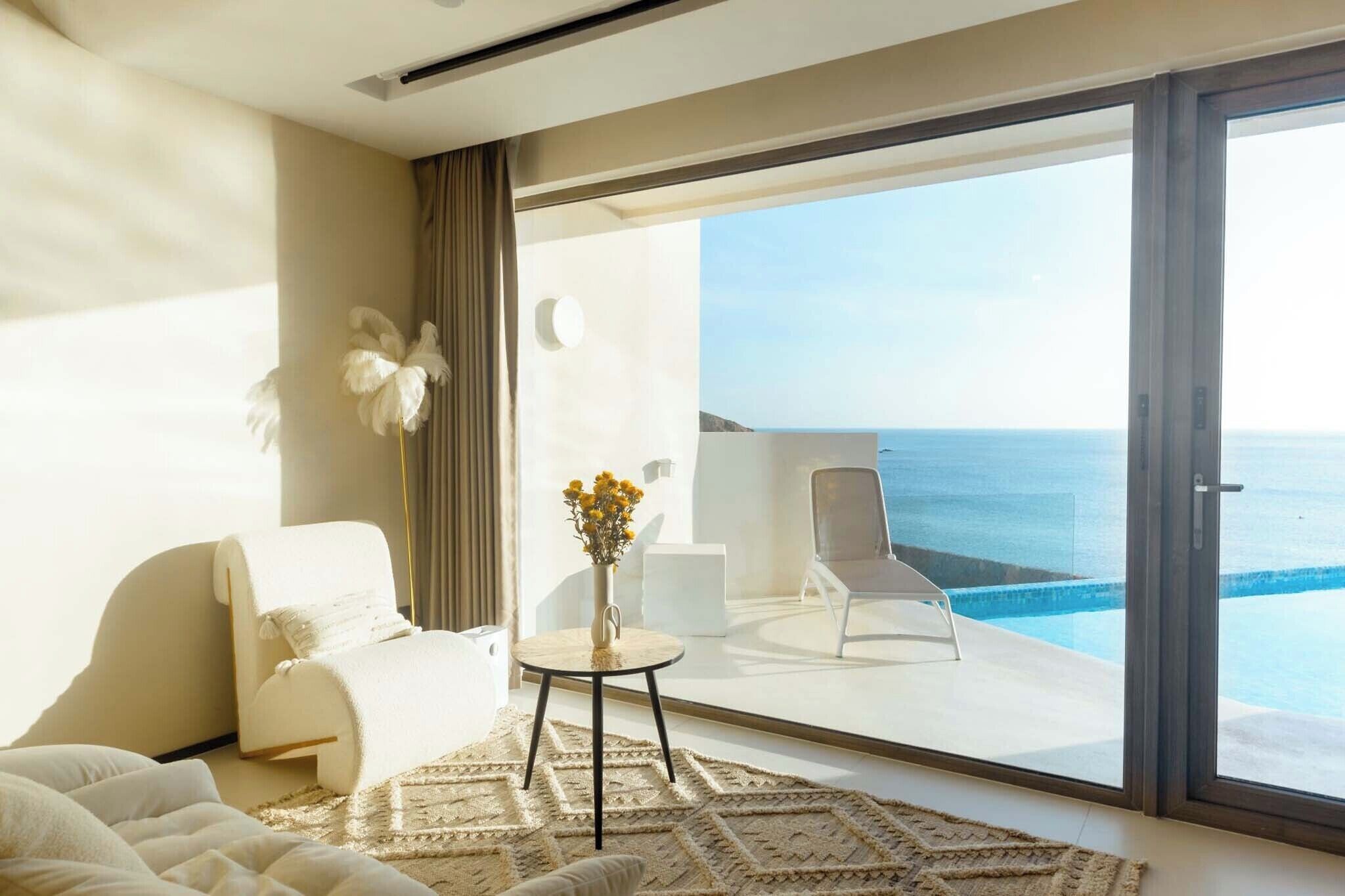 A modern hotel room with a large sliding glass door leading to a balcony with a view of the sea.