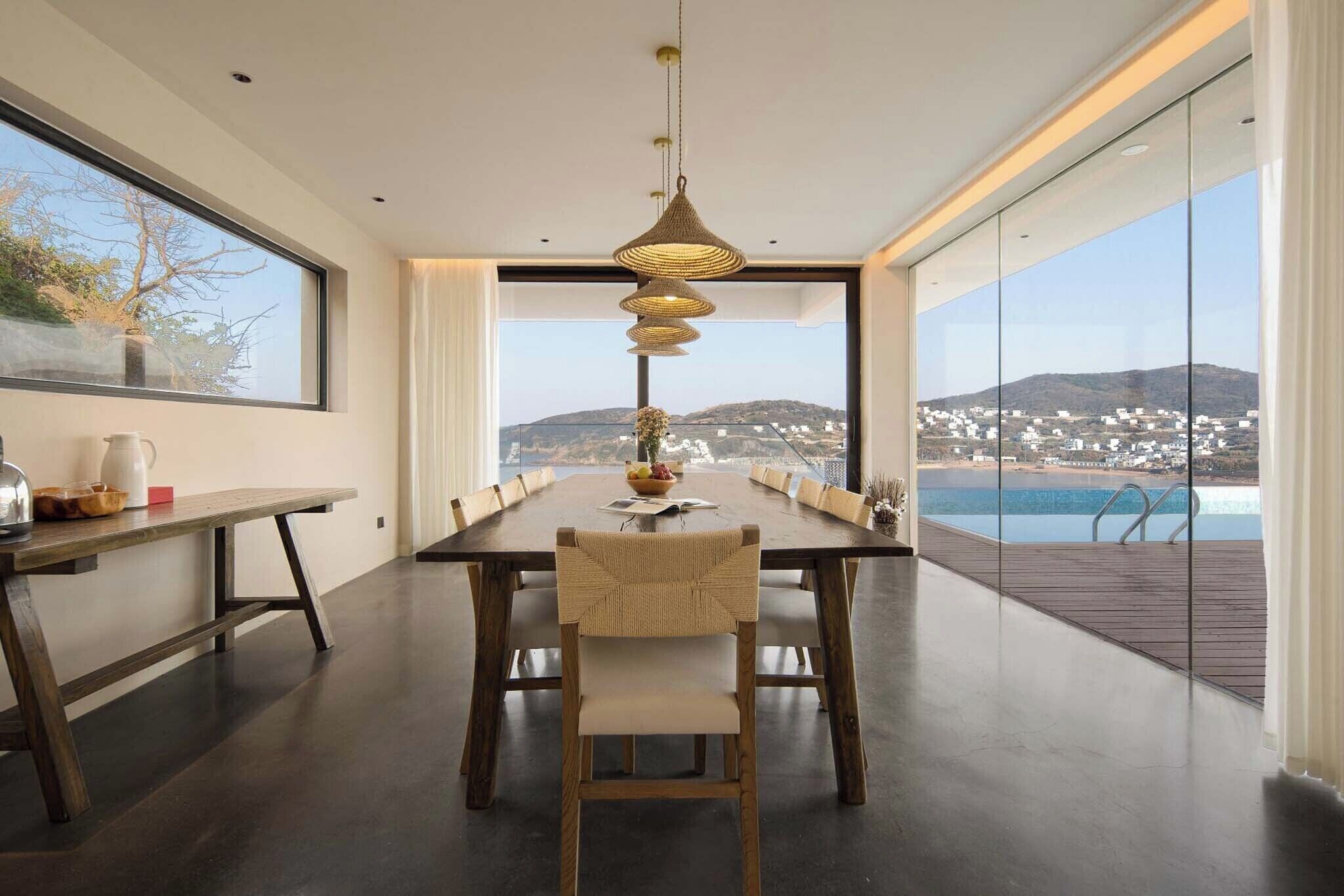 A modern dining room with a long table, chairs, and a hanging light fixture.