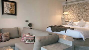 Una habitación de hotel moderna con un sofá, una cama con almohadas estampadas, una pared de piedra y una obra de arte enmarcada en la pared.