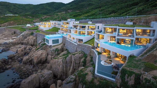 A modern multi-story hotel with a rooftop pool, situated on a rocky cliff overlooking a body of water. - XIHUI Cliff Hotel (Zhoushan)