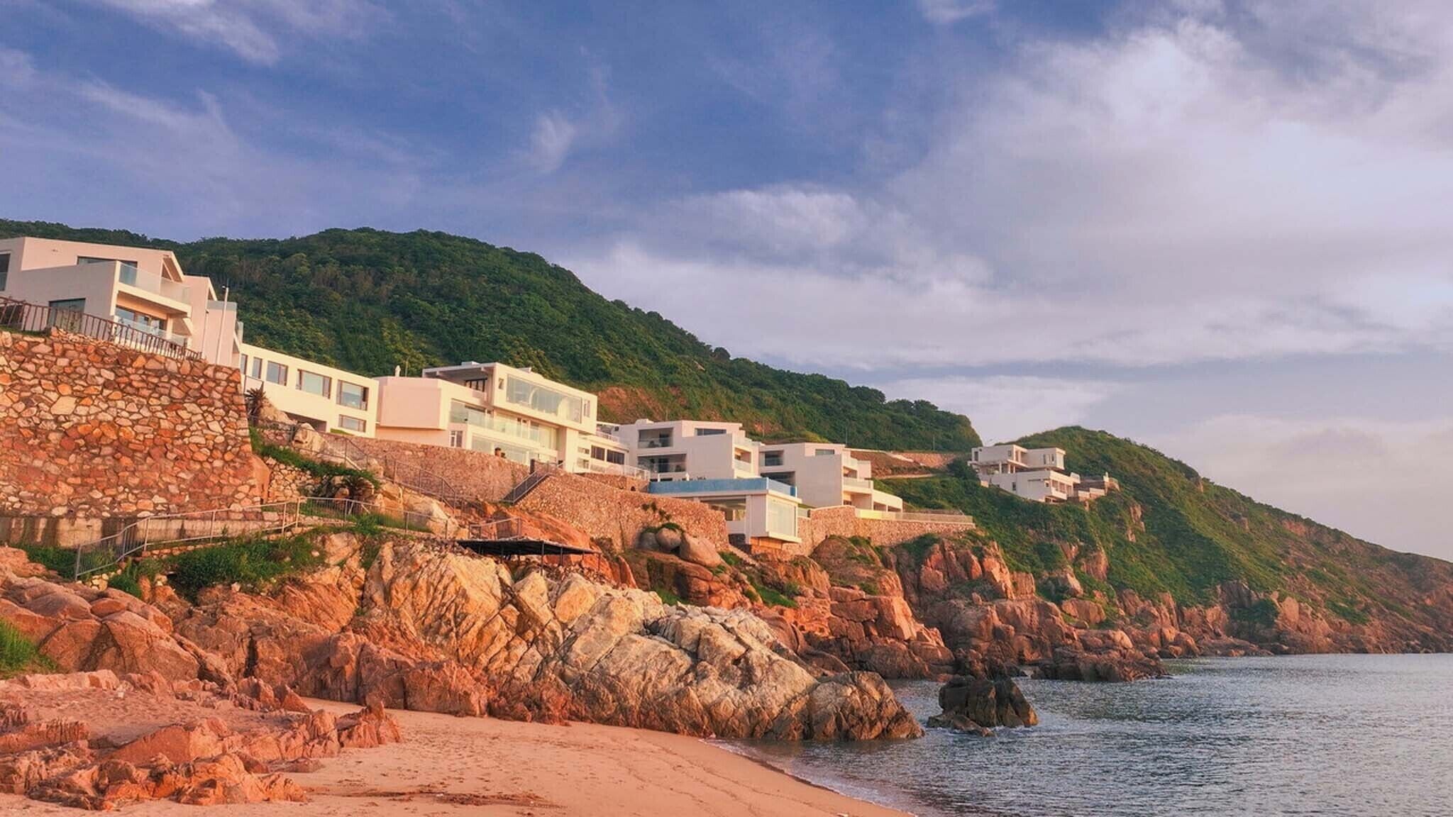 A coastal property with modern architecture, a rocky shoreline, and a view of the sea.