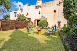 A courtyard with a wooden fence, a small table with chairs, and a building with a tiled roof and a round window. - Fort Galantè, Alghero, Italy (Alghero)