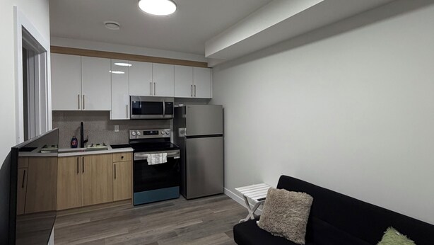 A modern kitchen with white cabinets, a black countertop, and a stainless steel refrigerator. - Cozy 2BR Suite Near NAIT | Wi-Fi + Kitchen (Edmonton)