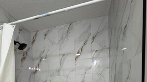 A bathroom with a white bathtub, marble-patterned walls, and a shower curtain. - Cozy 2BR Suite Near NAIT | Wi-Fi + Kitchen (Edmonton)