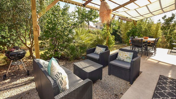 Una terrazza esterna con mobili in vimini, un barbecue e una zona coperta con una pergola.