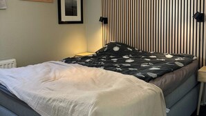 A bed with a patterned blanket, a bedside table, a wall-mounted lamp, a framed picture, and a radiator. - 5 Star Holiday Home in Uddevalla (Uddevalla)