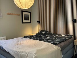 Una cama con una colcha estampada, una mesita de noche, una lámpara de pared, un cuadro enmarcado y un radiador.