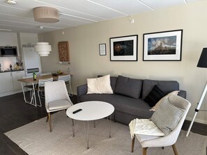 A modern living room with a grey sofa, two armchairs, a small white table, and a kitchen in the background. - 5 Star Holiday Home in Uddevalla (Uddevalla)