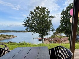 Una terraza de madera con una mesa y sillas, con vistas a un lago tranquilo con un muelle y casas al fondo.