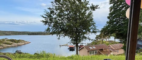 A wooden deck with a table and chairs, overlooking a lake with a dock and houses in the background.