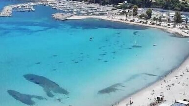 Une plage côtière avec une eau claire, un rivage sablonneux et une colline en arrière-plan.