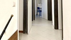 Un couloir avec une porte sur la gauche, une chaise au centre et un bureau avec une chaise à l’arrière-plan.