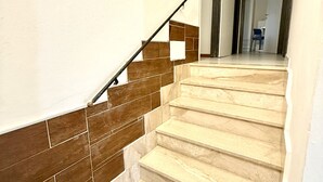 Un escalier aux marches beiges et aux murs recouverts de carreaux bruns, menant à une pièce où se trouvent une chaise et un bureau.