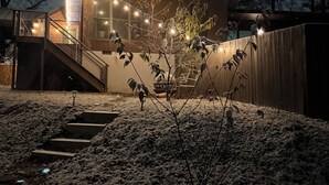 Ein modernes Haus mit Holzfassade, einer Treppe zu einer Terrasse und Lichterketten.