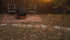 Ein Garten mit Holzzaun, zwei Metallstühlen, einer Feuerstelle und Lichterketten.