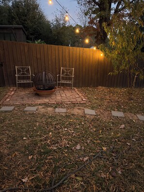 A backyard with a wooden fence, two metal chairs, a fire pit, and string lights. - Cozy Studio Downtown Raleigh (Raleigh)