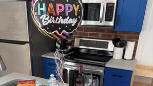Eine Küchenarbeitsplatte mit Geburtstagstorte, Luftballons, Snacks und einer Weinflasche.