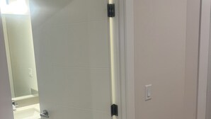 Eine weiße Tür mit Griff, Lichtschalter und einem kleinen Spiegel über einem Waschbecken.