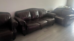Ein Wohnzimmer mit einem dunkelbraunen Ledersofa, einem passenden Sessel und einem kleinen Tisch mit Glasplatte.