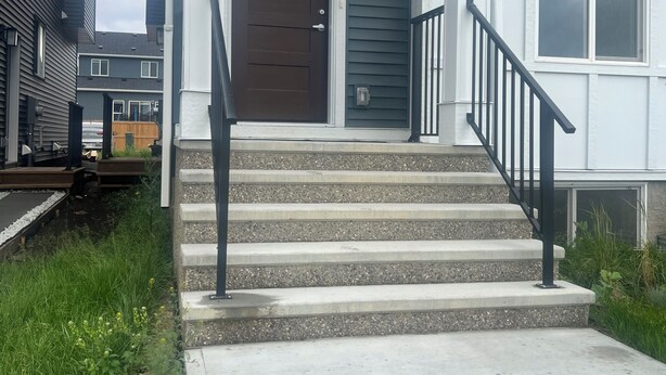 Ein Wohngebäude mit Eingangstür, einer Treppe mit Handlauf und einer kleinen Veranda.