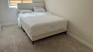 Ein Schlafzimmer mit einem Bett, einem Fenster mit Jalousien und einem Teppichboden.