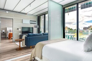 Una habitación de hotel moderna con una cama grande, un sofá azul, una mesita y un televisor.