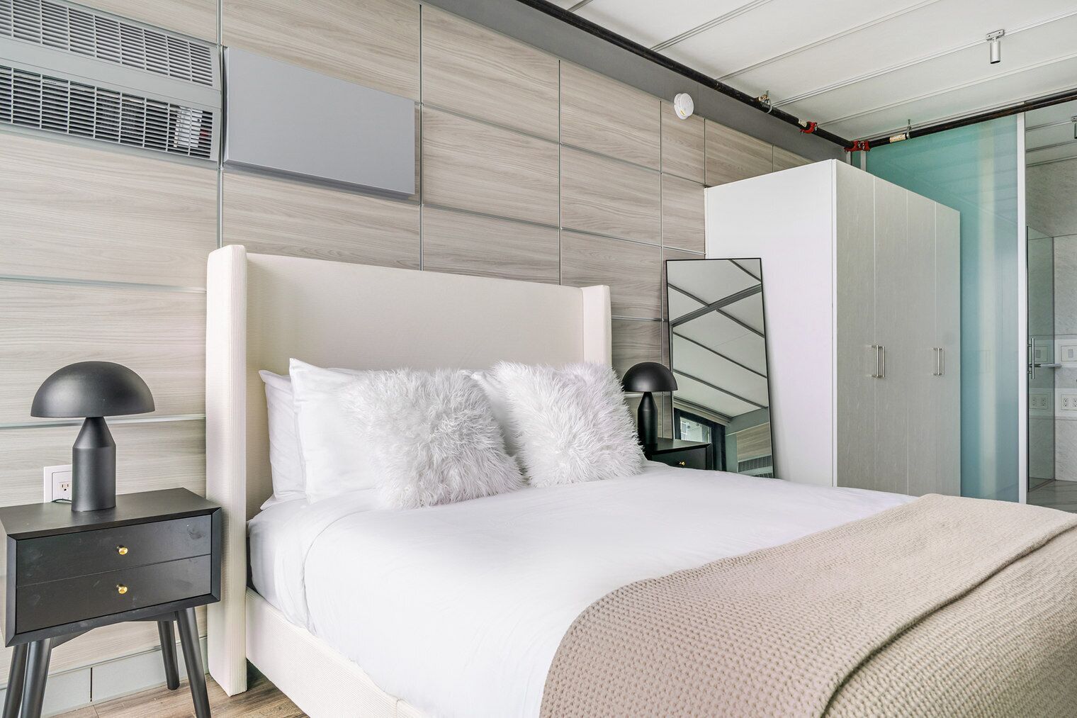 A modern bedroom with a bed, bedside tables, a wardrobe, and a mirror.