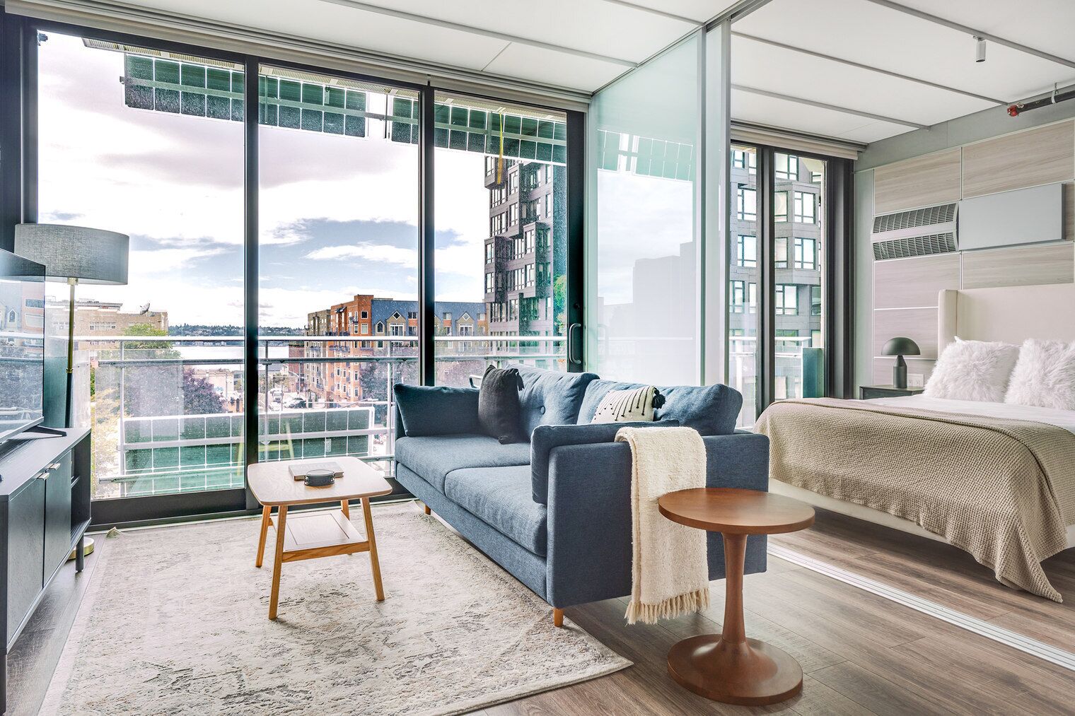 A modern apartment with a large balcony, a sofa, a bed, and a small table.