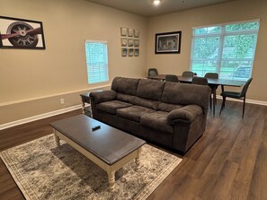 A living room with a brown sofa, a coffee table, a rug, a dining table with chairs, and framed pictures on the walls. - Spacious Home Near HSV Airport & Entertainment - Space & Rckt, Orion amp theatre (Madison)