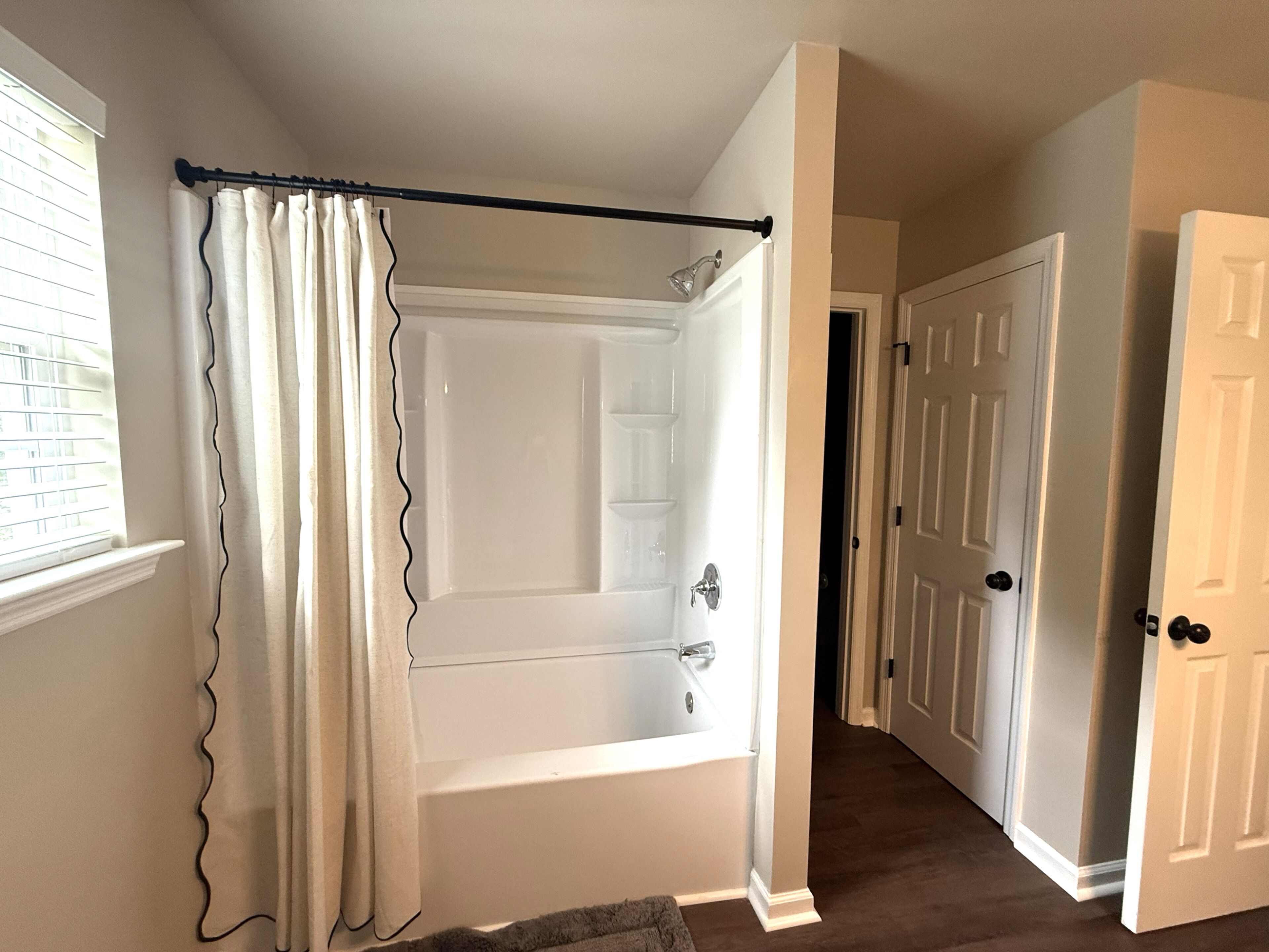 A bathroom with a bathtub, a shower curtain, and a door leading to another room.