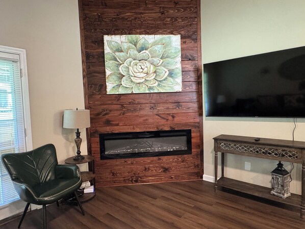A living room with a wooden wall, a fireplace, a television, a green leather chair, and a small table with a lamp. - Spacious Home Near HSV Airport & Entertainment - Space & Rckt, Orion amp theatre (Madison)
