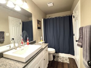 A bathroom with a white sink, a mirror, a toilet, and a shower curtain. - Spacious Home Near HSV Airport & Entertainment - Space & Rckt, Orion amp theatre (Madison)