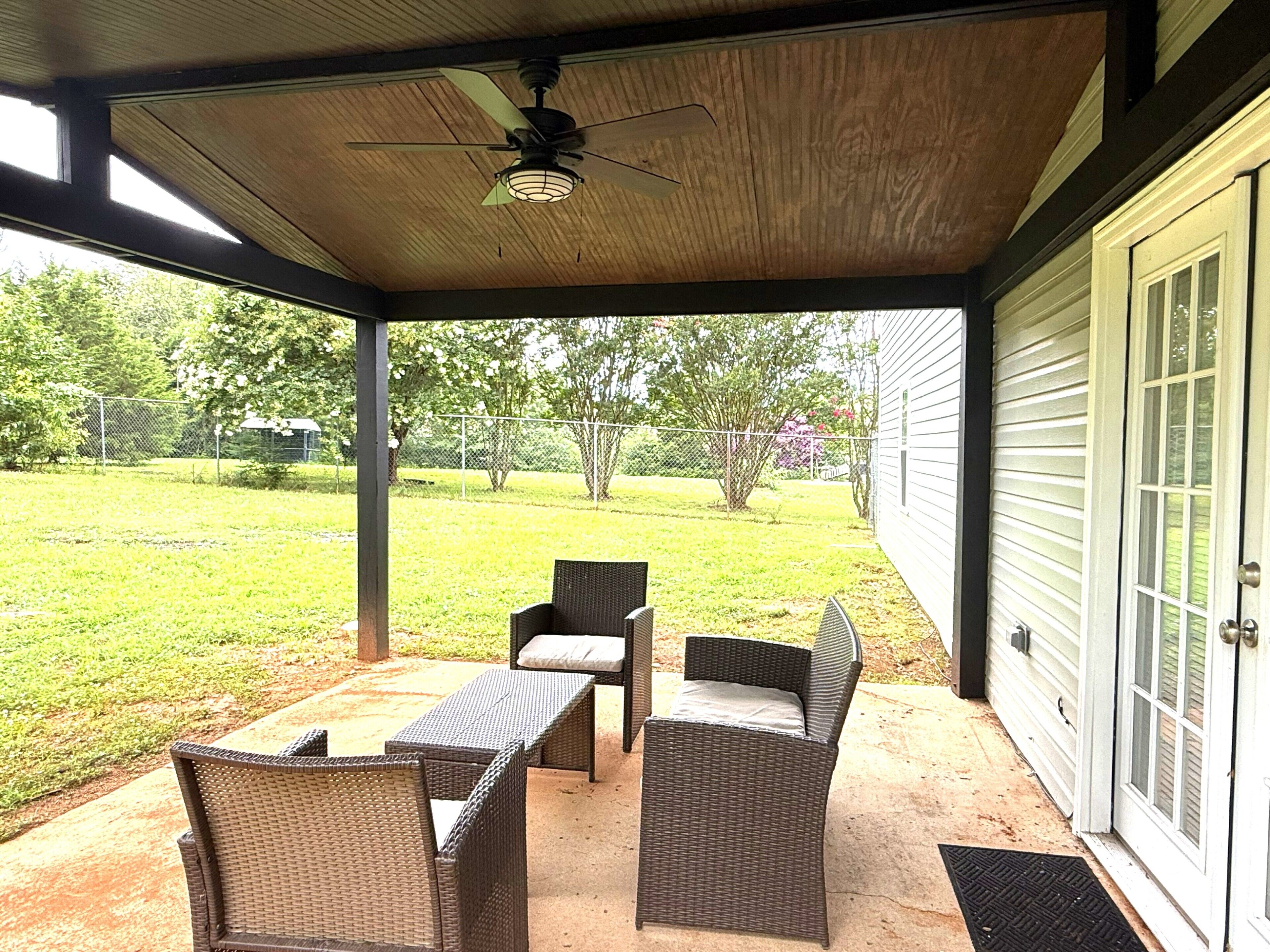 Un portico coperto con mobili in vimini, una ventola a soffitto e vista su un prato.