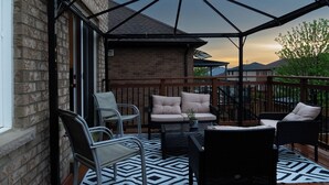 A covered outdoor patio with a brick wall, a wooden deck, and a seating area with chairs and a sofa. - Lake Getaway in Barrie (Barrie)