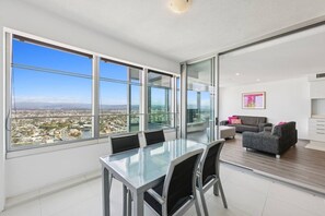 A modern apartment with large windows, a dining area, and a living space with a sofa and a painting. - level 32 Skyline Serenity in Surfers Paradise Q1 (Surfers Paradise)