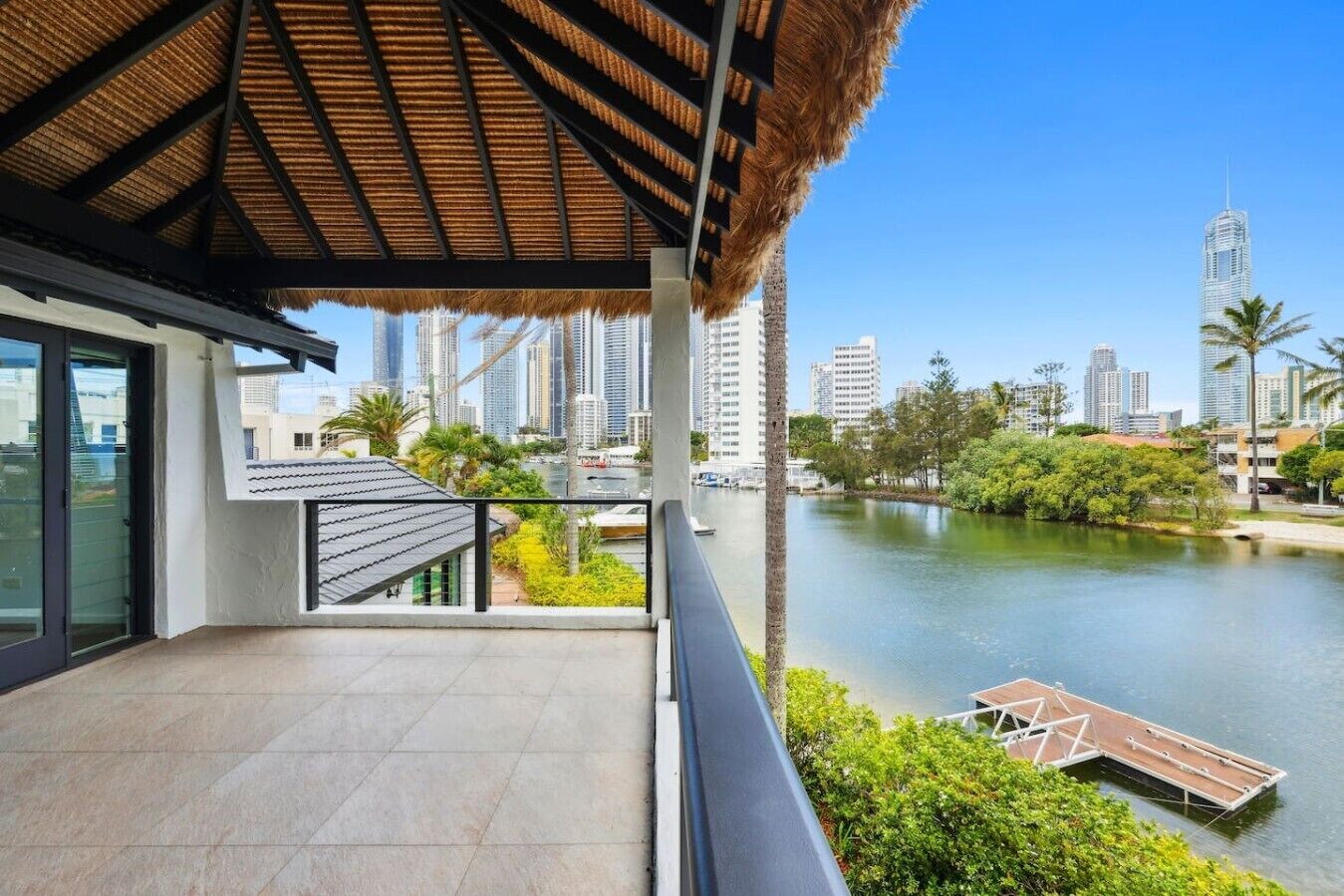 A modern building with a thatched roof balcony overlooking a body of water and a cityscape.