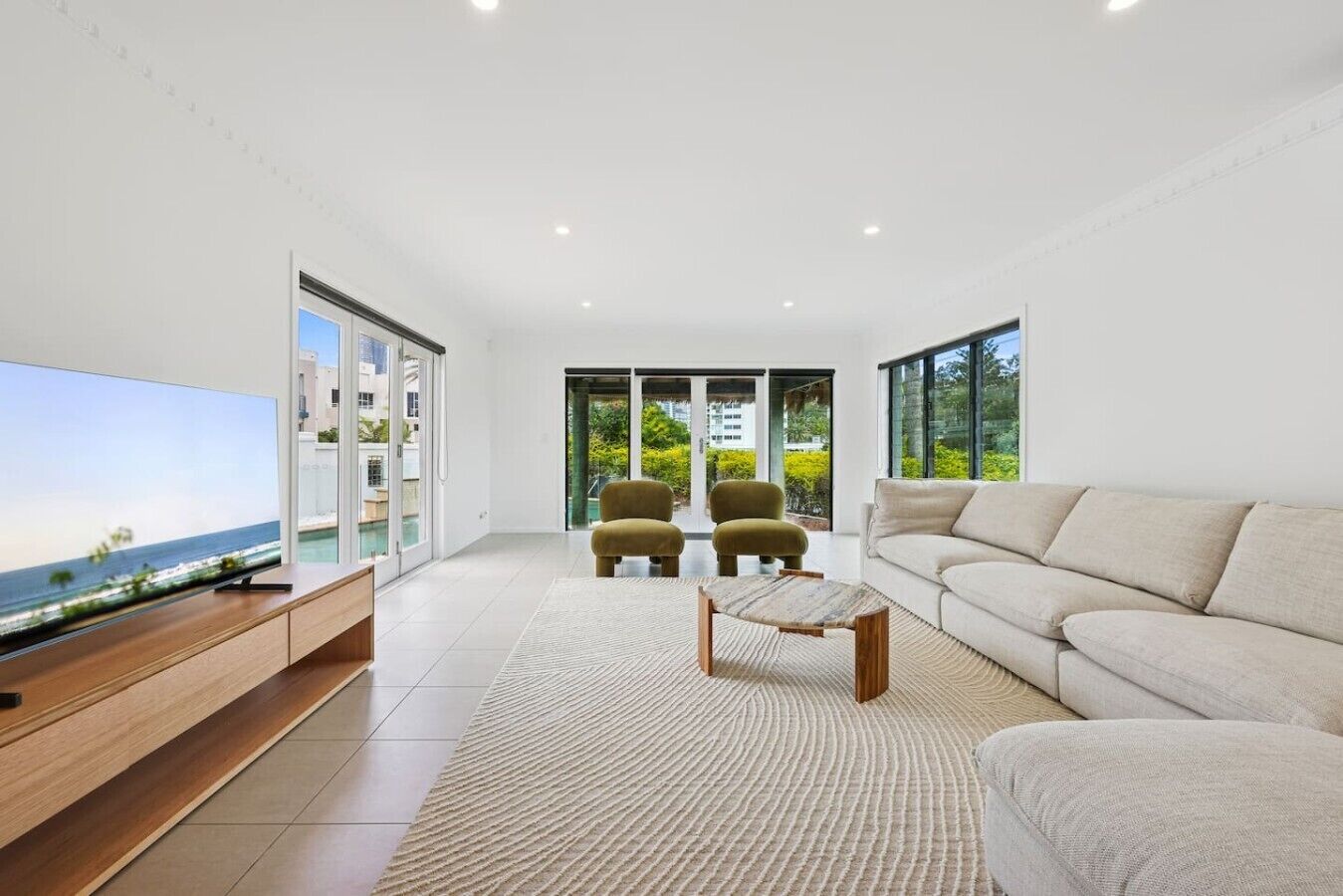 A modern living room with a flat-screen TV, a beige sofa, two armchairs, and a coffee table.
