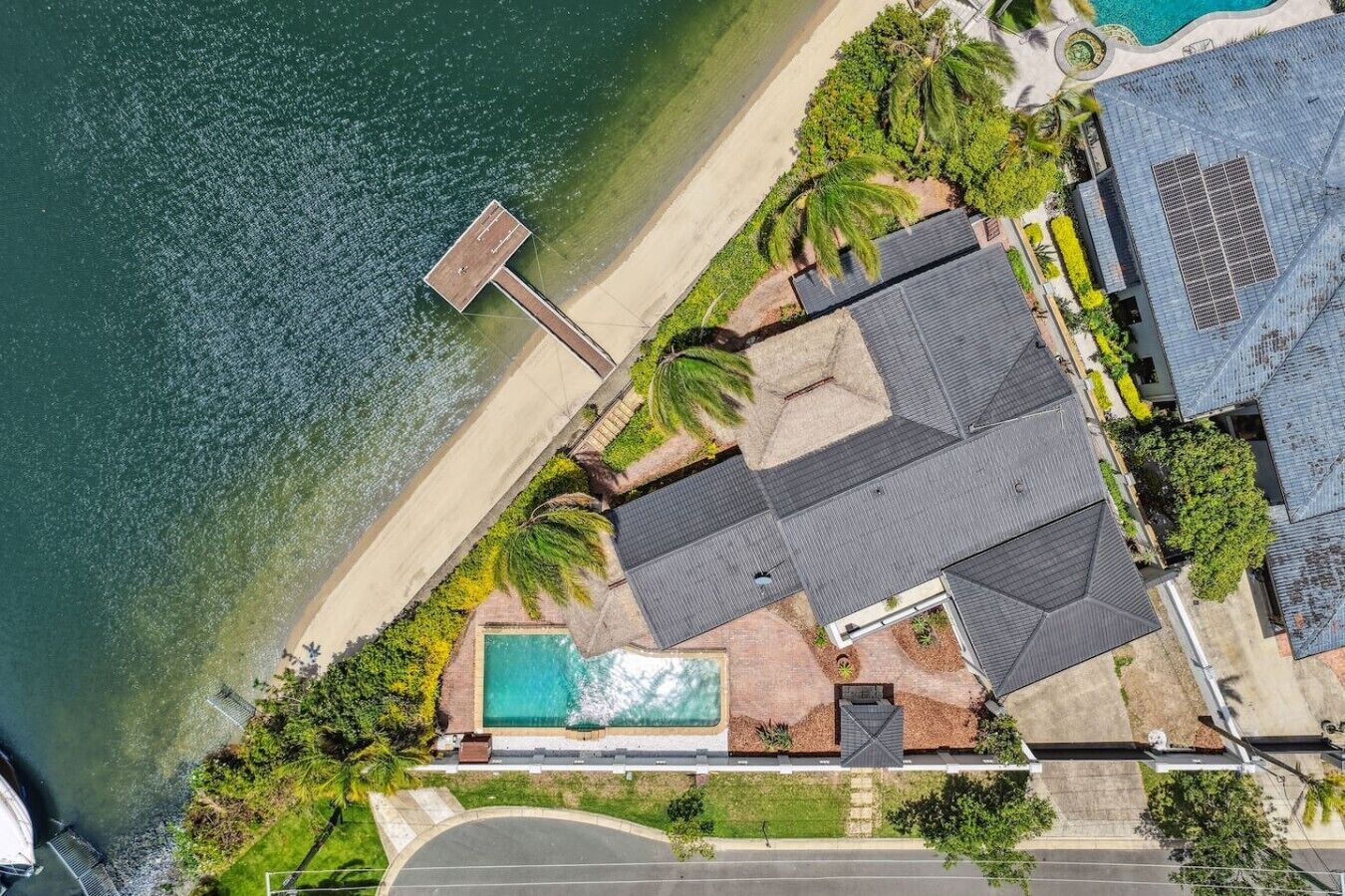 Vue aérienne d’une propriété située sur la côte, avec une piscine, un quai et une grande maison dotée d’un toit en pente.