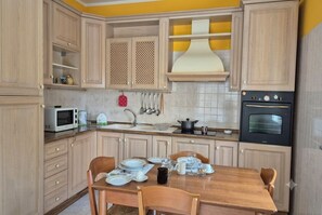A kitchen with wooden cabinets, a microwave, a stove, and a dining table set with plates and glasses. - Enjoy a spacious 90sqm Apartment, 5 Mins from Beach and Bus stop to Taormina (Giardini Naxos)