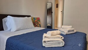 Uma cama bem arrumada com um edredom azul, travesseiros brancos e uma pilha de toalhas brancas.