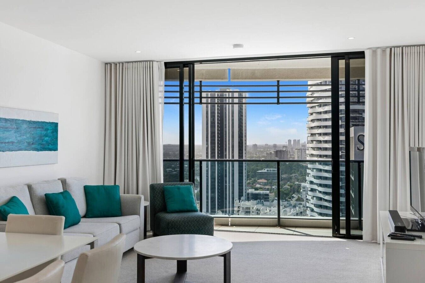 Een moderne hotelkamer met een ruim balkon, een bank, een stoel, een tafel en een schilderij aan de muur.